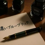 木製デスクの上に置かれたペリカンM400万年筆と、濃いブルーブラックインクで試し書きされた紙。